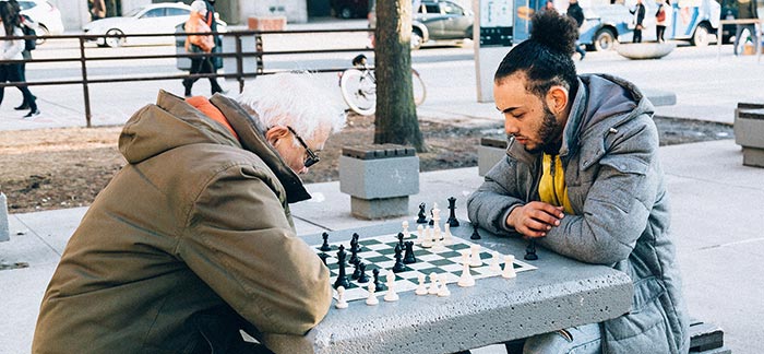 senior man and younger man playing chess outside in park