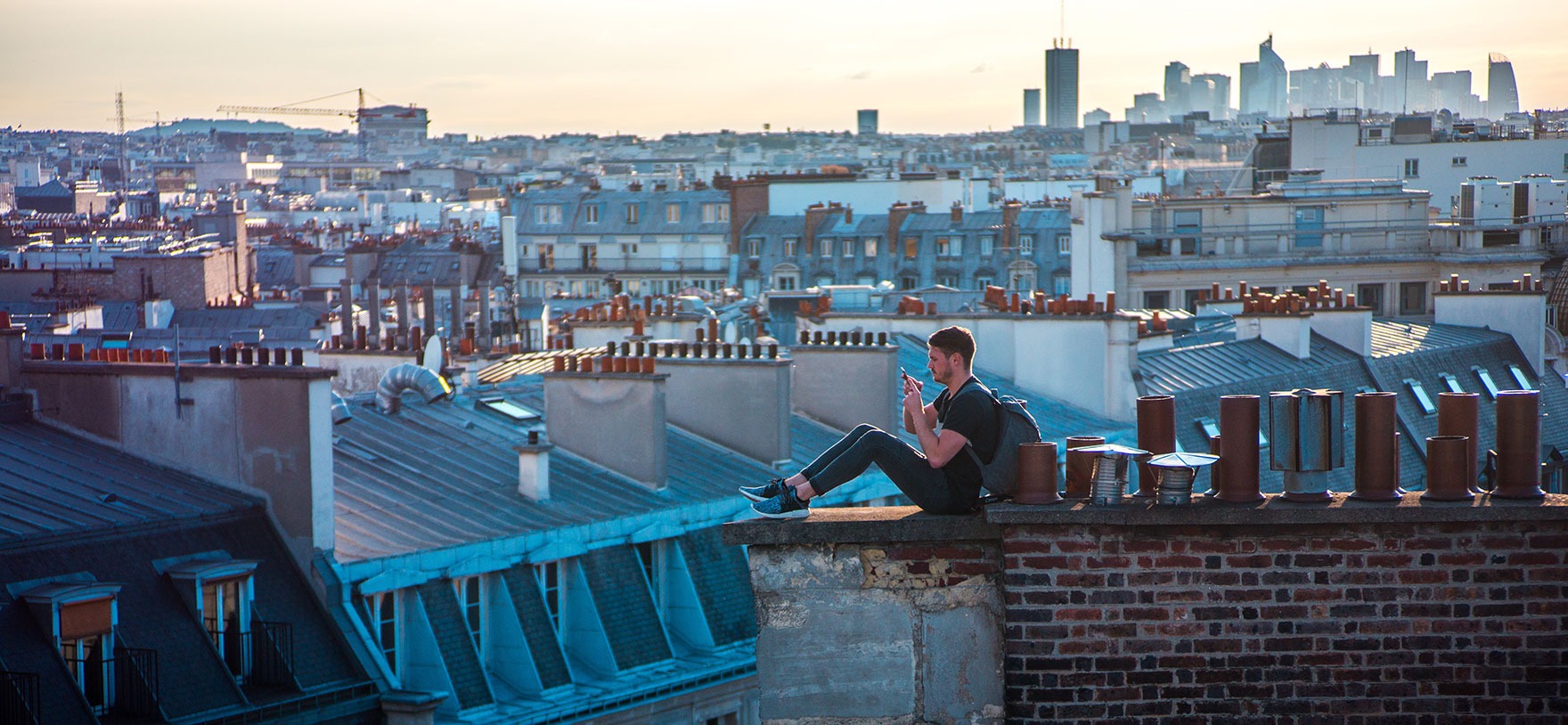 Image of young man sitting on a rooftop using his smartphone