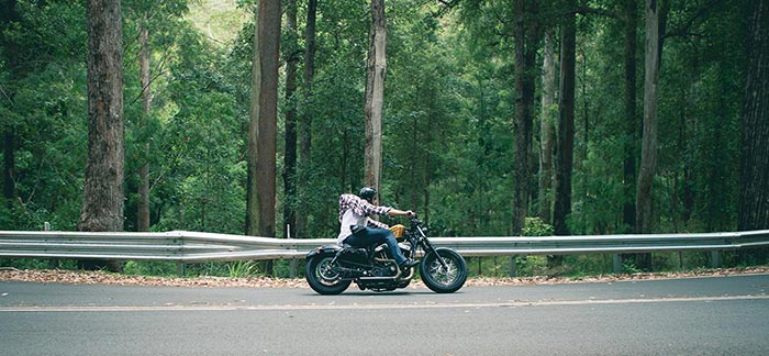 Image of man riding motorcycle on a road next to a forest for Quotacy blog Types of Life Insurance Riders.