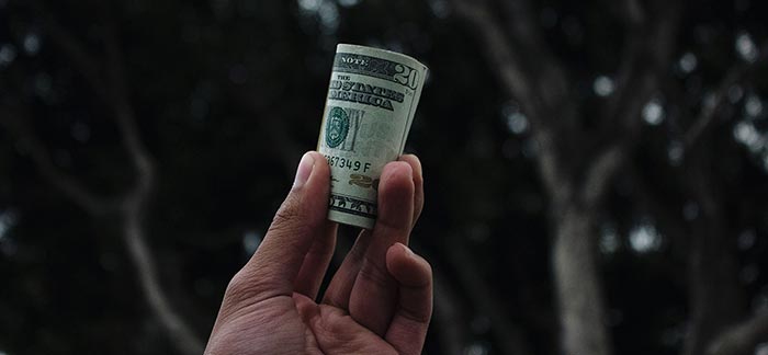 Image of hand holding rolled up twenty dollar bill for Quotacy blog 7 Ways to Save on Life Insurance.