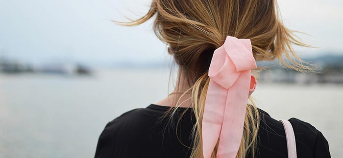 Image of woman with pink bow in her hair looking at a sandy beach for Quotacy blog Cancer and Life Insurance.