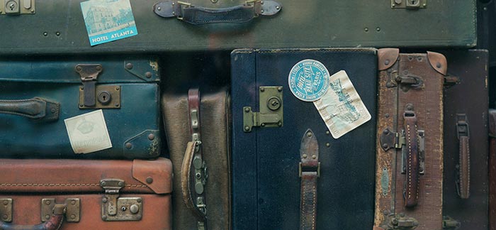 Image of stacked antique suitcases covered in travel stickers for Quotacy blog Protecting Yourself While Traveling.