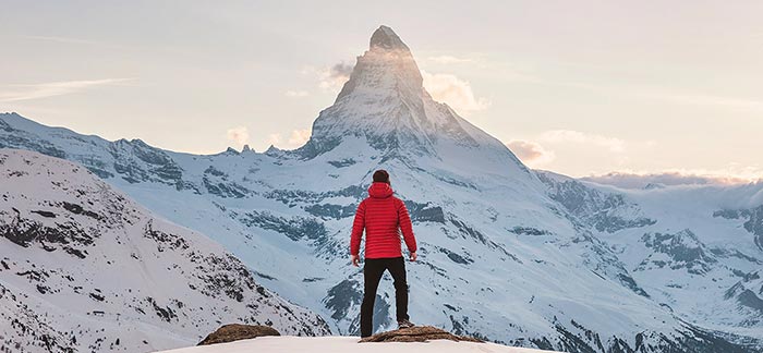 Image of a hiker looking at a mountain peak while standing on a cliff for Quotacy blog Setting and Achieving Financial Goals.