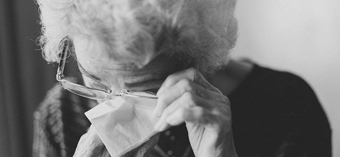 Image of senior woman wiping her eyes with tissues and crying for Quotacy blog Elder Financial Abuse.