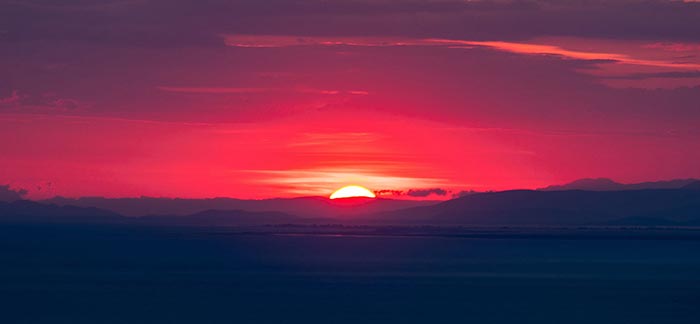 Image of beautiful red sunset over the ocean horizon for Quotacy blog The Optimism Bias and Life Insurance.