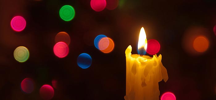 Image of lit candle burning in front of colorful orbs of light for Quotacy blog Discussing Family Legacy During the Holidays.