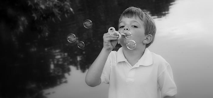 Image of little boy blowing bubbles in front of a pond