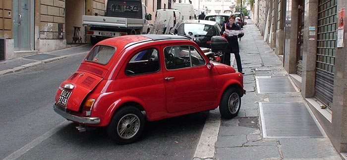 Image of small, red car parked crooked on a sidewalk for Quotacy blog Common Life Insurance Mistakes to Avoid.