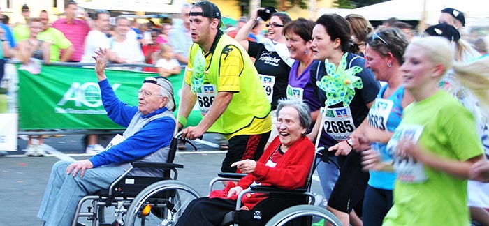Image of two seniors in wheelchairs being pushed by runners in a marathon for Quotacy blog Who Needs Life Insurance More?