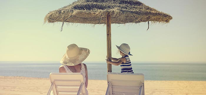 Image of mom & daughter under a beach umbrella to block the sun for Quotacy blog Life Insurance & Skin Cancer: Buyer's Guide.