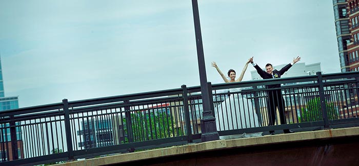 Image of two newlyweds celebrating with arms waving overhead on a bridge for Quotacy blog Financial To-Dos for Newlyweds.