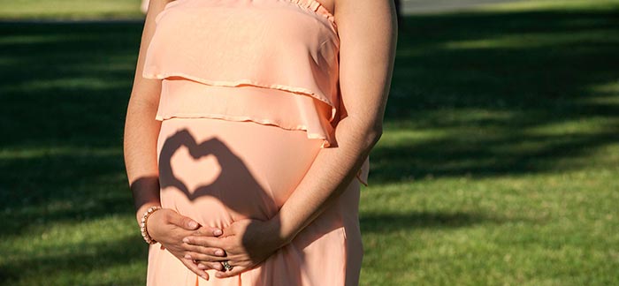 Image of pregnant mom with hand shadows making heart shape on belly for Quotacy blog Getting Life Insurance While Pregnant.