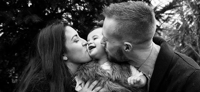 Image of happy toddler being kissed by mom and dad for Quotacy blog Money Saving Tips for New Parents.