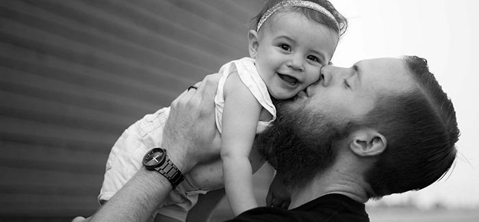 Image of young dad holding his baby daughter and kissing her on the cheek for Quotacy blog The Importance of Life Insurance for Dads.