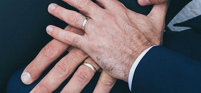 Image of 2 men's hands overlapping with wedding rings on their fingers for Quotacy blog Estate Planning for Same-Sex Couples.