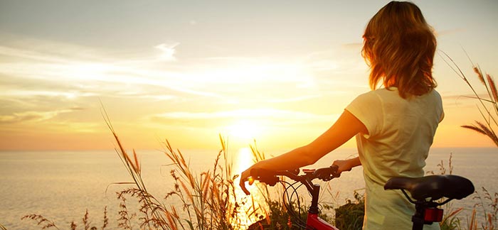 Image of woman standing with a bike looking at the sunset for Quotacy blog Life Insurance & Colorectal Cancer: Buyer's Guide