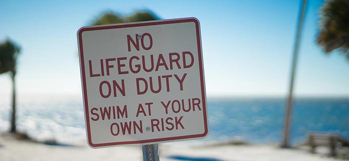 Image of beach sign that says no lifeguard on duty swim at your own risk for Quotacy blog What Is Life Insurance Underwriting