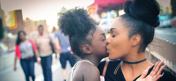 mom and daughter kissing each other's cheeks on bustling city street for Quotacy blog Can a Minor Be a Beneficiary?