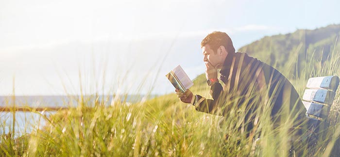 Image of man reading book on bench in front of lake for Quotacy newsletter Rest, Relaxation, and a Really Great Shower.