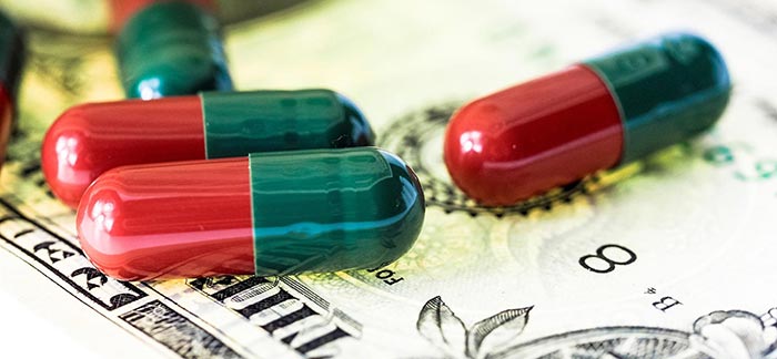 Image of prescription pills sitting on top of a dollar bill for Quotacy blog Health Insurance and Your 2016 Tax Returns.