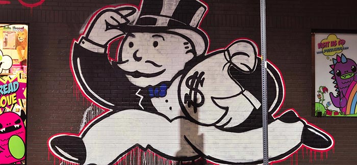 Spray-painted graffiti on a wall of Uncle Pennybags from Monopoly for Quotacy blog: How Much Life Insurance Can I Get.