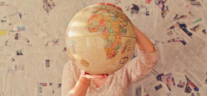 Image of woman with globe in front of face & newspaper wallpaper for Quotacy newsletter Feed a Cold Starve a Fever? Maybe Not