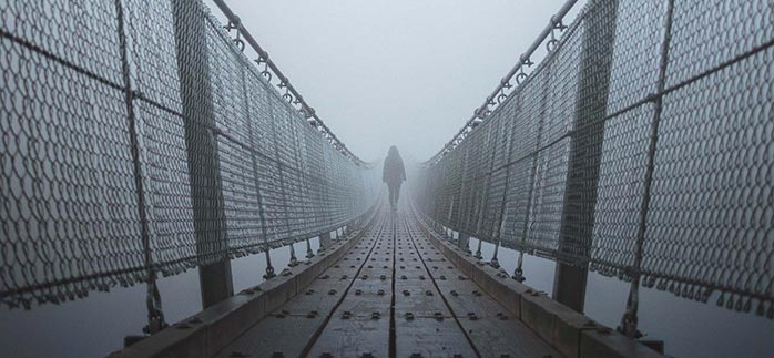Image of woman walking alone over a misty hanging bridge for Quotacy blog Alcohol Abuse and Life Insurance.