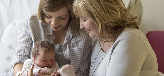 Image of mom holding her newborn baby with smiling grandmother for Quotacy blog The Perfect Age to Buy Life Insurance.