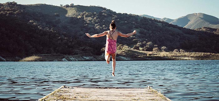 Image of young girl jumping off a dock into a lake for Quotacy blog Summer Safety Tips for Parents.