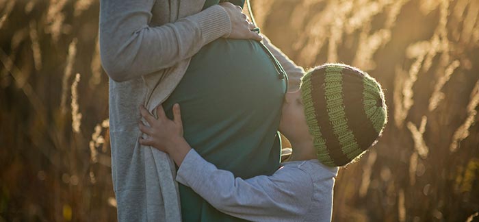 Image of young boy kissing his pregnant mother's belly for Quotacy blog How Does Pregnancy Affect Life Insurance Rates?