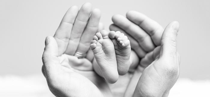 parent cupping their newborn baby's feet in black and white