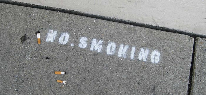 Image of spray-painted no smoking sign with three cigarette butts for Quotacy blog: Thinking About Quitting Smoking.