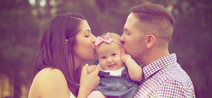 Image of mom and dad kissing newborn for Quotacy blog: How to Find the Best Term Life Option for New Families.