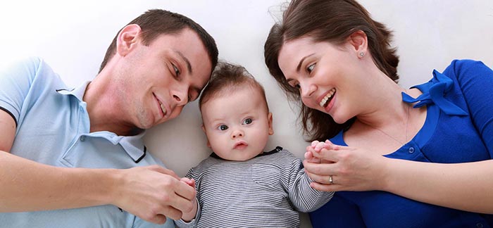 Image of mom, dad, and baby laying together for Quotacy blog Choose Between Term Life Insurance & Whole Life Insurance Quotes
