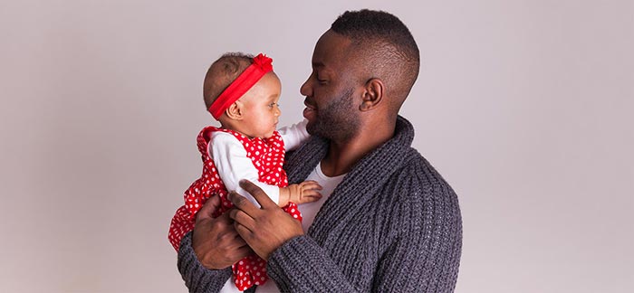 young father holds his baby daughter in his arms for Quotacy blog Why New Fathers Should Compare Term vs. Whole Life Insurance