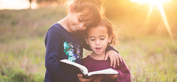 young sisters reading to each other in a sunny yard