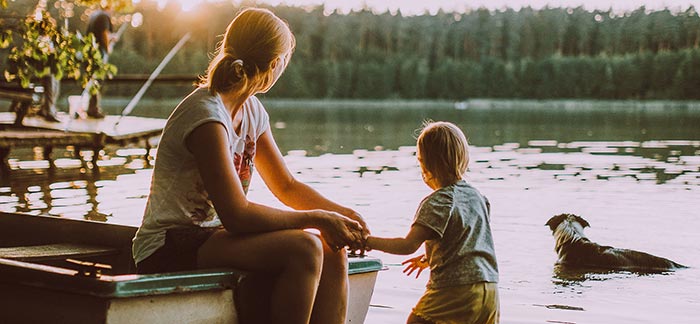 Image of woman sitting on a boat on the lake holding her toddler's land for Quotacy blog How Do Life Insurance Payouts Work?