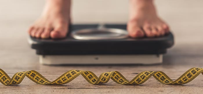 Image of a person standing on a scale with a measuring tape.