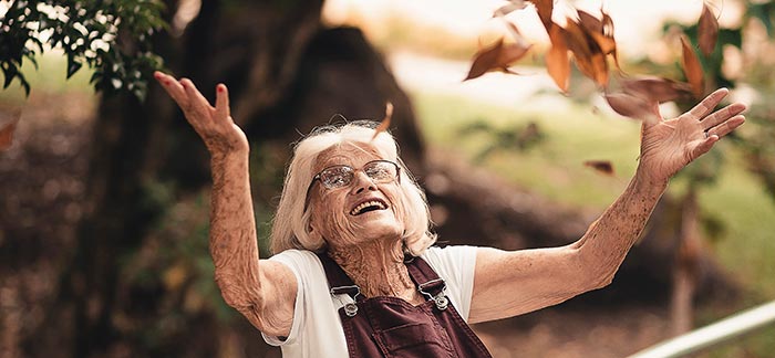 happy elderly woman throwing fall leaves for Quotacy blog How Will You Pay for Long-Term Care?