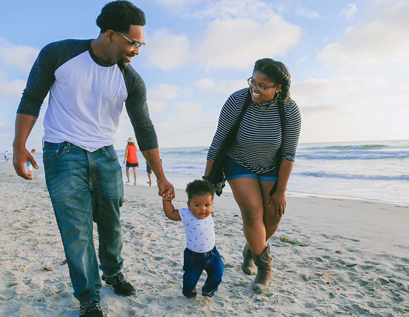 cost_life_insurance_child_rider_2 Mom, dad and baby walking along a sandy beach.