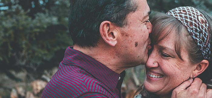 older man kissing wife on forehead for Quotacy blog cash value life insurance in retirement