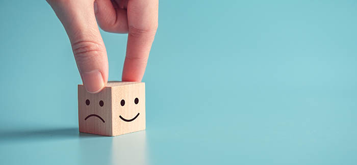 Person holding block with happy and sad faces for Quotacy blog What is toxic positivity and how can it be harmful
