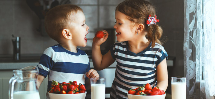 toddler sister feeding toddler brother a strawberry