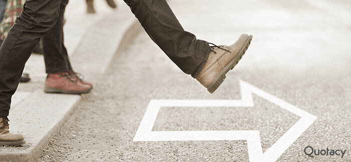 Persons legs stepping on to a paved street with an arrow pointing forward on the ground