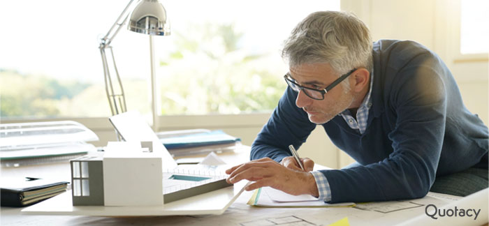 older professional man in navy sweater and glasses working over his desk