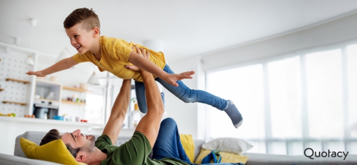 Image of a father laying on his back on a couch lifting his young son up in the air.