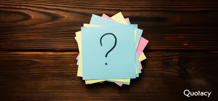 Image of pink, yellow, and blue sticky notes messily stacked on top of each other sitting on a wooden table top. The one on the top of the stack is blue with a black question mark on it.