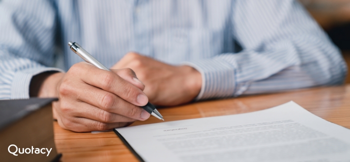 Man in a blue and white striped dress shirt at a wood table signing a document