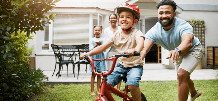 dad teaching his young son how to ride a bike in their backyard